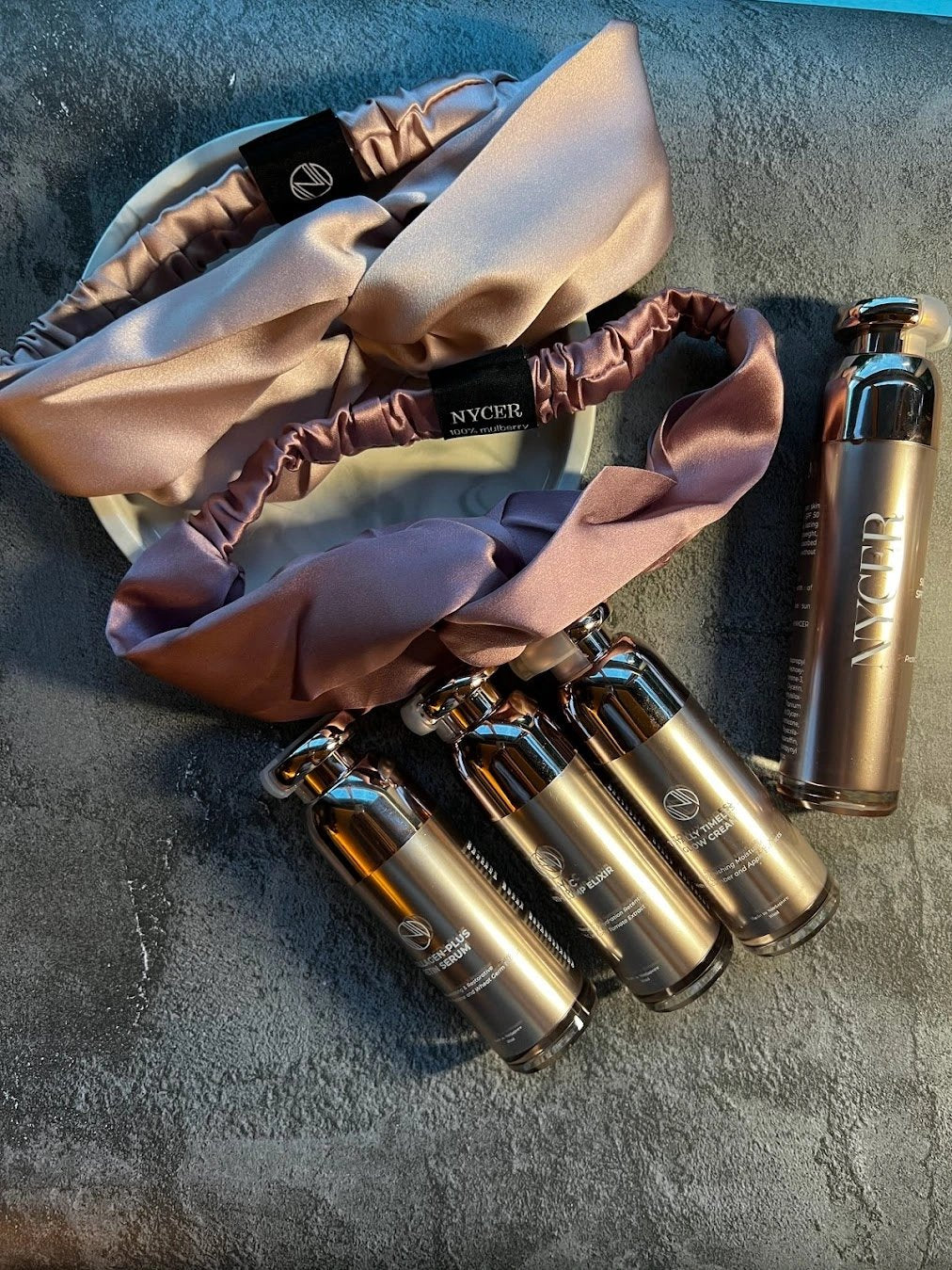 100% Mulberry Silk Headband in Mauve and Dusty Pink. Next to rose champagne bottles of skincare. On a marble tray